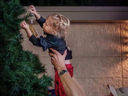 A father lifts his daughter to place her ornament on the Cuero Christmas tree.