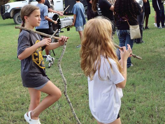 Young girls practice making music next to the Wildcat Band, using sticks as instruments.