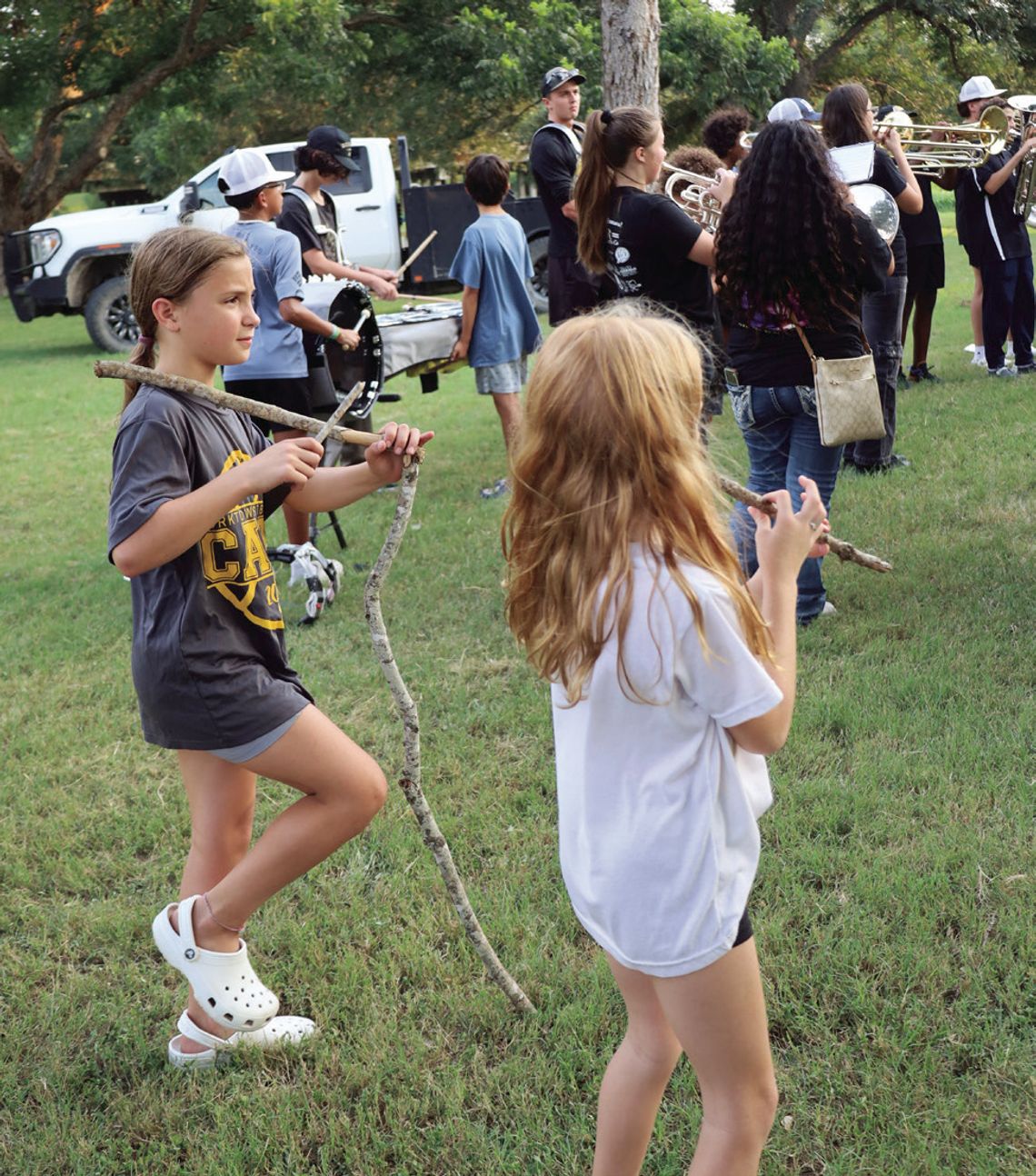 Young girls practice making music next to the Wildcat Band, using sticks as instruments.